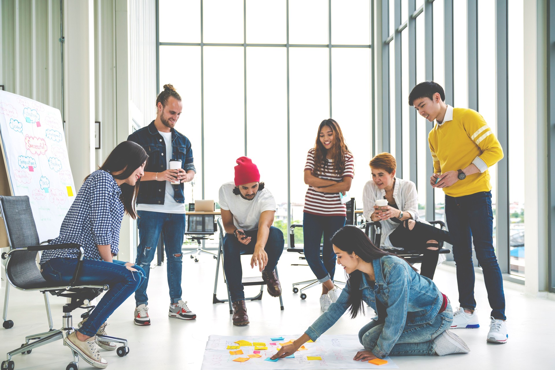 Young creative diverse group meeting and looking at project plan lay out on floor discuss or brainstorm business strategy with post note. Workshop for startup team in modern office. Happy workplace.